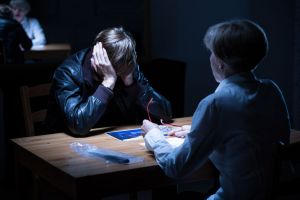 A young offender without a juvenile defense attorney is seen covering their ears during a police interrogation